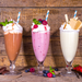 Three delicious milkshakes topped with whipped cream, berries, and caramel dessert topping on wooden background.