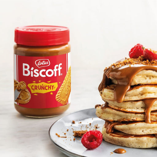 Lotus Biscoff crunchy biscuit spread jar next to stacked pancakes topped with crunchy Biscoff spread and fresh raspberries